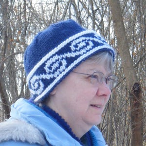 May include: A blue knitted hat with a white patterned design. The hat has a white band with a swirling pattern.