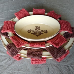 Pode incluir: Um conjunto de três pratos de cerâmica com um design floral castanho e branco. Os pratos estão envoltos em panos de cozinha de malha castanho e vermelho.