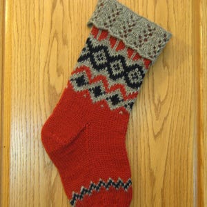 May include: A red knitted Christmas stocking with a black and gray geometric pattern. The stocking has a gray knitted cuff.
