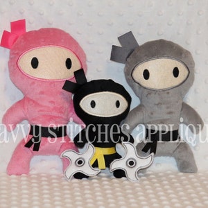 May include: Three plush ninja toys, one pink, one gray, and one black. The pink ninja has a pink bow on its head. The gray ninja has a gray headband. The black ninja has a yellow belt and is holding two white ninja stars.