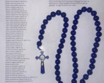 Peut inclure: Un chapelet composé de perles bleu foncé, d'un crucifix argenté avec des accents en émail bleu et d'une petite médaille ovale. Le chapelet est présenté sur une feuille de papier blanche imprimée avec le texte de la litanie de la Vierge.