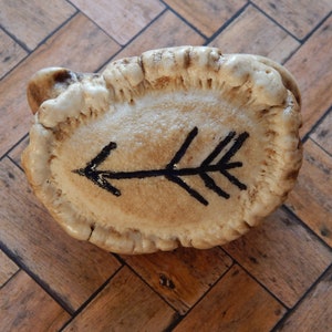 Może przedstawiać: Biały poroże z narysowaną na nim czarną strzałą. Poroże leży na drewnianej powierzchni.