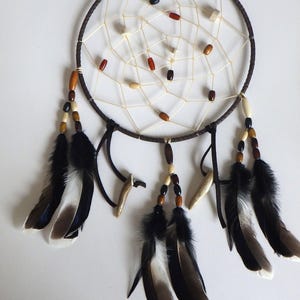 May include: A brown dreamcatcher with a white web and brown, red, and black beads. It has black feathers with white tips hanging from the bottom.