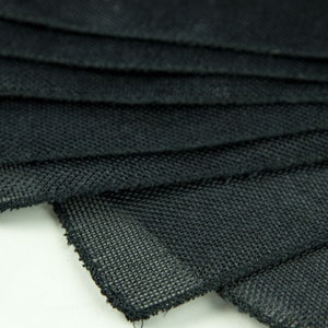 May include: Close-up of black mesh fabric folded in layers. The fabric has a fine, even weave and a slightly textured surface.