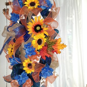 May include: A fall-themed door wreath with orange, blue, and brown mesh, sunflowers, and blue flowers.