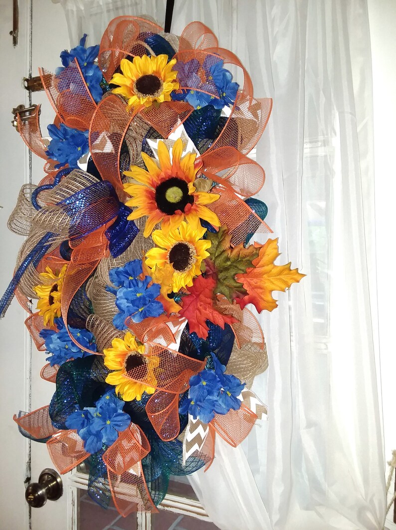May include: A fall-themed door wreath with orange, blue, and brown mesh, sunflowers, and blue flowers.