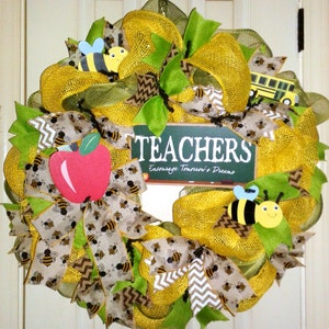May include: A decorative wreath with a school theme. The wreath features yellow and green mesh, ribbons with bee patterns, and a sign that says "TEACHERS". It also includes a red apple and a yellow school bus.