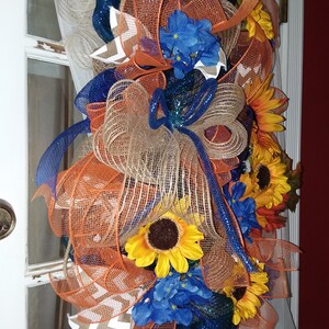 May include: A wreath with orange, blue, and brown mesh ribbon, accented with sunflowers and blue hydrangeas.