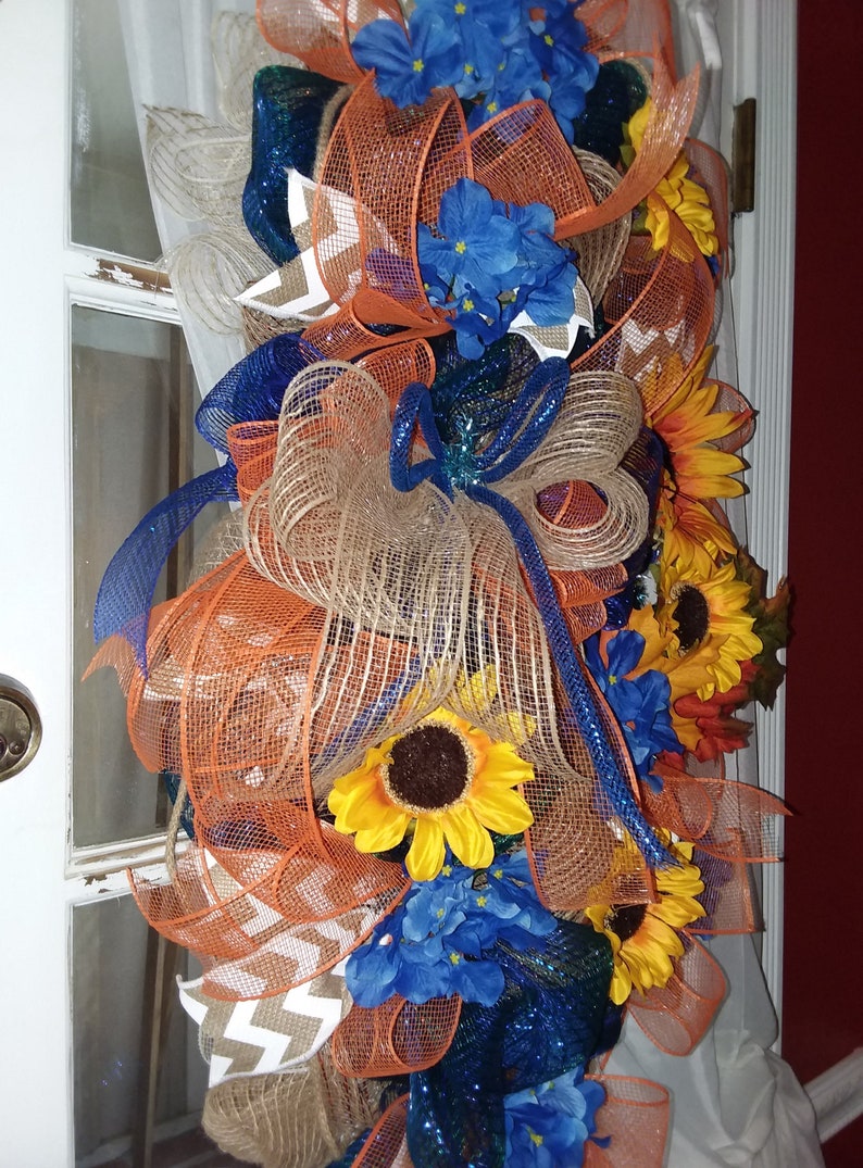 May include: A wreath with orange, blue, and brown mesh ribbon, accented with sunflowers and blue hydrangeas.