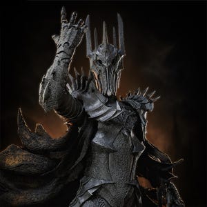 May include: A dark gray armored figure wearing a tall, spiked helmet and textured plate armor. The figure has one arm raised with a gauntlet featuring sharp, pointed details. A flowing, dark, textured cape extends from the shoulders.