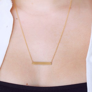 May include: A gold bar necklace with a delicate chain. The bar pendant is simple and sleek.