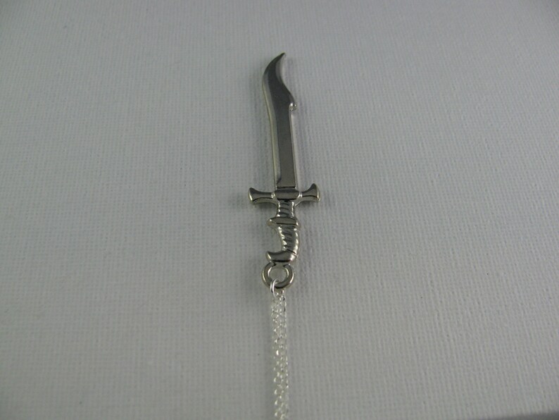 May include: A silver sword pendant necklace with a detailed design. The sword has a curved blade and a decorative handle.