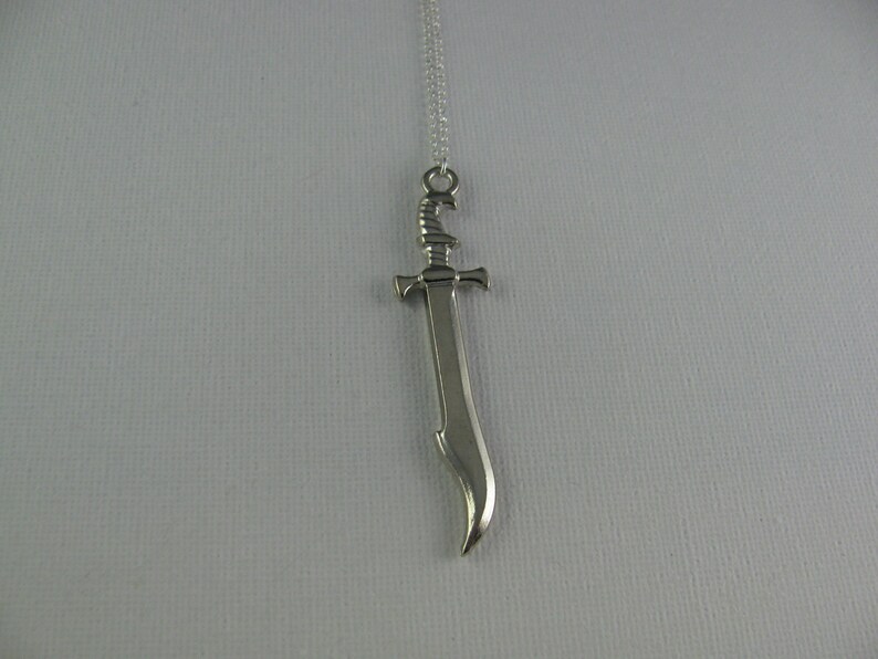 May include: A silver sword pendant necklace. The sword has a curved blade and a detailed hilt.