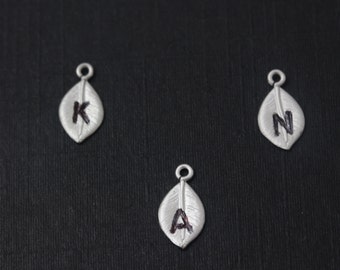 May include: Three silver leaf charms with the letters K, A, and N engraved on them.