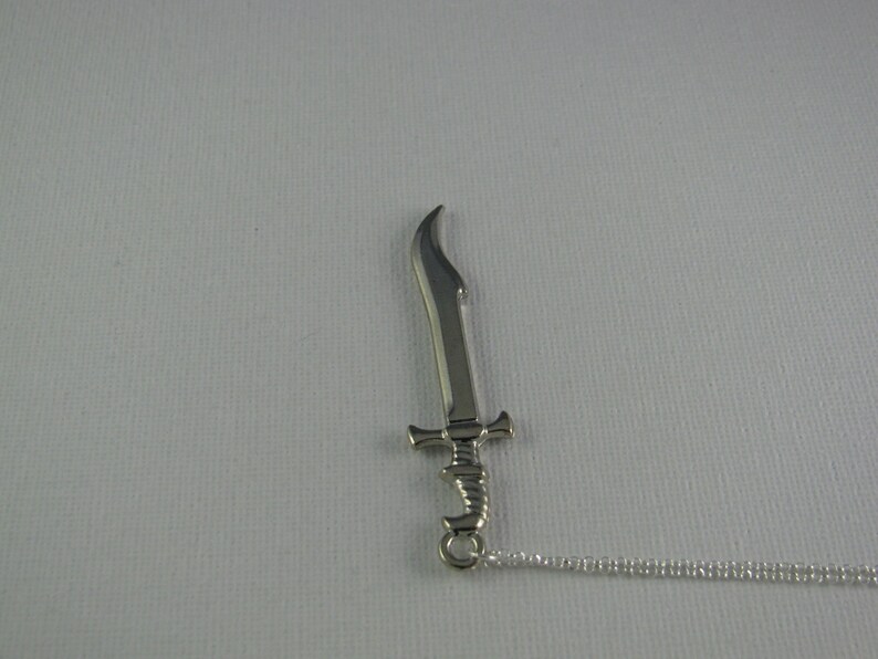 May include: A silver sword pendant necklace with a chain. The sword has a curved blade and a detailed hilt.