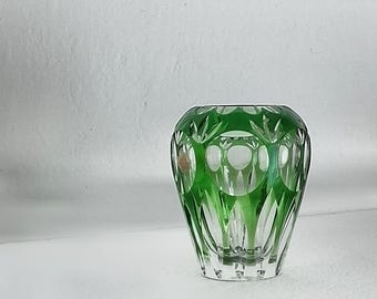 Puede incluir: Un jarrón de vidrio tallado en verde y transparente que presenta una serie de patrones circulares y en forma de hoja grabados en la superficie exterior. El diseño alterna entre secciones de color verde esmeralda y vidrio.