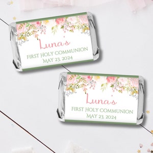 May include: Two green and white favor labels with pink floral designs. The labels read "Luna's First Holy Communion May 23, 2024".