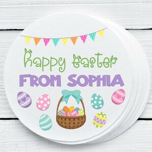 May include: Round white sticker with a colorful Easter theme. It features a basket of Easter eggs, a banner with flags, and the text "Happy Easter from Sophia".