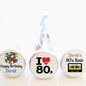 May include: Three foil-wrapped candies with custom labels. One features a Rubik's Cube and "Happy Birthday Derek." Another says "I love the 80s" with a heart. The third says "Derek's 80's Bash" with a cassette tape graphic.