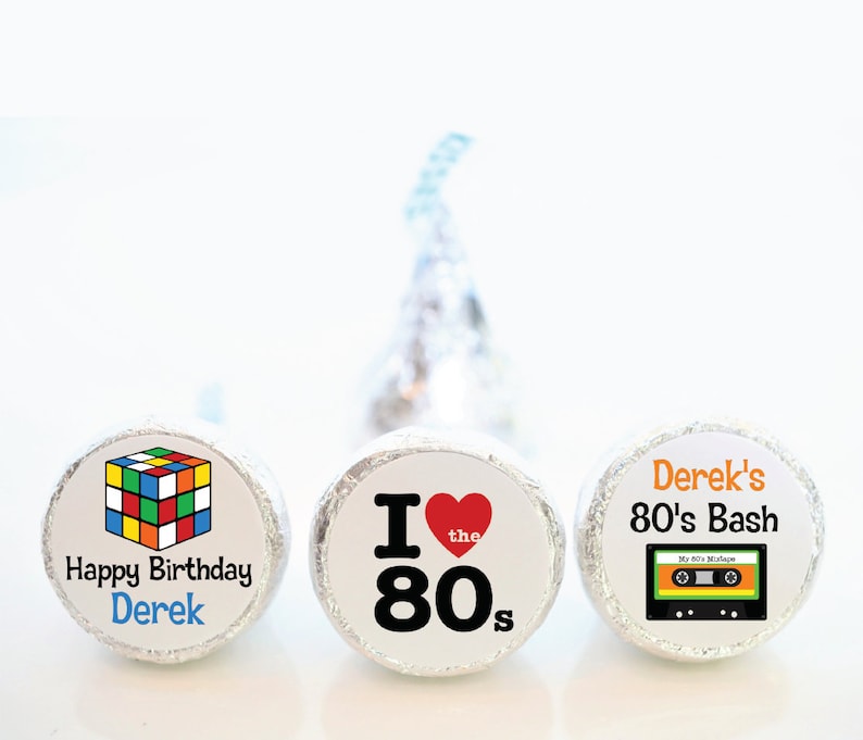 May include: Three foil-wrapped candies with custom labels. One features a Rubik's Cube and "Happy Birthday Derek." Another says "I love the 80s" with a heart. The third says "Derek's 80's Bash" with a cassette tape graphic.