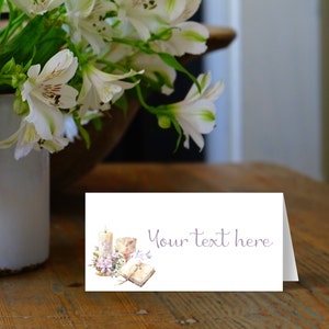 May include: A white card with a watercolor illustration of a candle, a chalice, a book, and flowers. The text "Your text here" is printed in purple on the card.