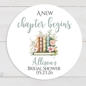May include: A round white sticker with the text "A New Chapter Begins" in a script font. The sticker features a watercolor illustration of books and flowers. The text "Allison's Bridal Shower 05.23.26" is also included.