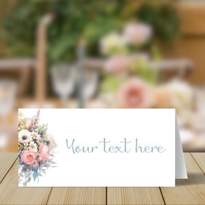 May include: A white place card with a floral design on the left side and the text "Your text here" in blue script on the right side.