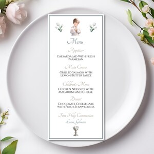 May include: A white menu card with a blue border, featuring a watercolour illustration of a young boy in a white robe. The menu lists the food options for a First Holy Communion celebration, including Caesar salad, grilled salmon, chicken nuggets, chocolate cheesecake, and the name "Liam Gilmore".