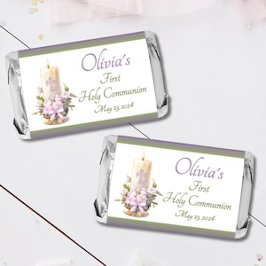 May include: Two silver foil-wrapped chocolate bars with personalized labels. The labels are white with a green border and feature a candle with a cross, flowers, and the text "Olivia's First Holy Communion May 23, 2024".