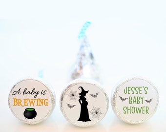May include: Three round, silver-colored chocolate candies with Halloween-themed labels. The first label says "A baby is brewing" with a black cauldron. The second label has a silhouette of a pregnant witch with bats and spiderwebs. The third label says "Jesse's Baby Shower" with bats.