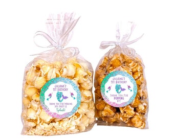 May include: Two clear cellophane bags filled with popcorn, tied with white ribbon. One bag has white popcorn with a mermaid-themed sticker that says "Juliana's 1st Birthday Thank You for Making My Party a Splash!" The other bag has caramel popcorn with a mermaid-themed sticker that says "Juliana's 1st Birthday Thank You for Popping By!"