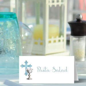May include: White place card with a blue cross and chalice design. The text "Pasta Salad" is written in blue cursive.