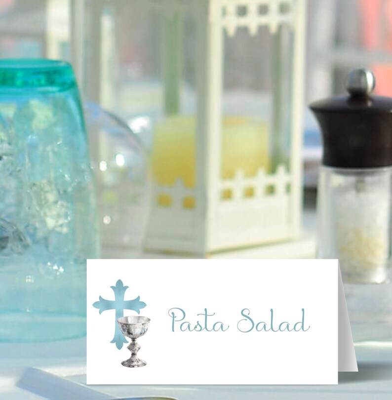 May include: White place card with a blue cross and chalice design. The text "Pasta Salad" is written in blue cursive.