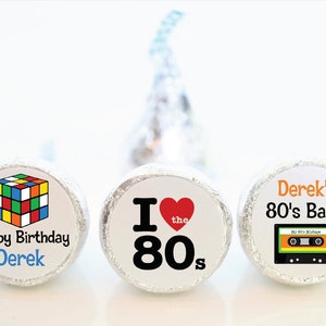 May include: Three foil-wrapped candies with custom labels. One features a Rubik's Cube graphic and "Happy Birthday Derek." Another says "I ❤️ the 80s." The last says "Derek's 80's Bash" with a cassette tape graphic.