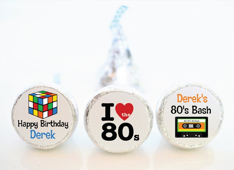 May include: Three foil-wrapped candies with custom labels. One features a Rubik's Cube graphic and "Happy Birthday Derek." Another says "I ❤️ the 80s." The last says "Derek's 80's Bash" with a cassette tape graphic.