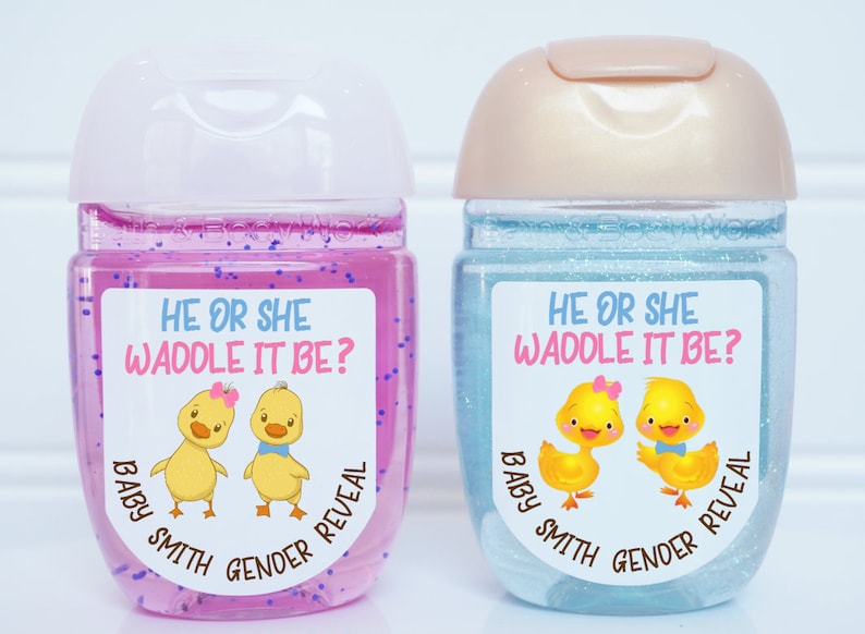 May include: Two clear plastic bottles with pink and blue glitter inside. Each bottle has a sticker with a cartoon duck couple and the text "He or She Waddle It Be? Baby Smith Gender Reveal".