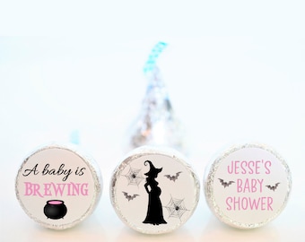 May include: Three round, silver-colored chocolate wrappers with Halloween-themed baby shower labels. The first label says "A baby is brewing" with a pink cauldron. The second label has a silhouette of a pregnant witch with bats and spiderwebs. The third label says "Jesse's Baby Shower" with bats.