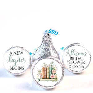May include: Silver foil-wrapped chocolate candies with custom labels. One label reads "A New Chapter Begins" in script. Another features a stack of books with floral accents. The third label says "Allison's Bridal Shower 05.23.26".