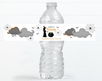 Könnte beinhalten: Ein weißes Wasserflaschenetikett mit einer schwarzen Hexensilhouette, einem Kessel und Fledermäusen. Der Text lautet "A baby is brewing" und "Elizabeth's Baby Shower".