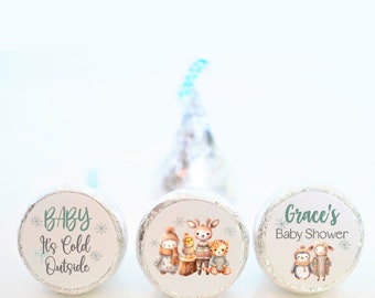 May include: Three round chocolate favor labels with winter-themed designs. One label says "Baby It's Cold Outside" with snowflakes. Another label features a penguin, a deer, and a tiger wearing winter clothes. The third label says "Grace's Baby Shower" with two penguins wearing winter clothes.