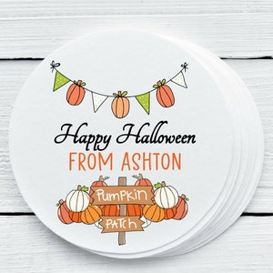 Può includere: Etichetta rotonda bianca con un tema di zucca. Dice "Happy Halloween from Ashton" e ha uno striscione di zucche e bandiere. C'è un cartello che dice "Pumpkin Patch" con zucche intorno.