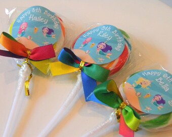 May include: Three colorful lollipops with mermaid-themed labels. Each lollipop has a different name and age on the label: Hailey 8th Birthday, Riley 5th Birthday, and Bella 6th Birthday. The lollipops are wrapped in clear cellophane and tied with colorful ribbons.