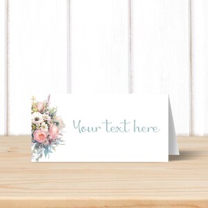May include: A white place card with a floral design in shades of pink, white, and green. The text "Your text here" is printed in light blue on the card.