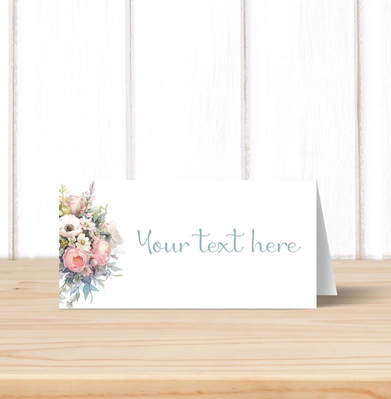 May include: A white place card with a floral design in shades of pink, white, and green. The text "Your text here" is printed in light blue on the card.