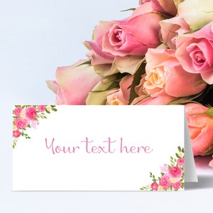 May include: A white card with pink floral borders and the text "Your text here" in pink script. The card is placed in front of a bouquet of pink roses.
