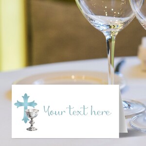 May include: A white place card with a blue watercolor cross and chalice design. The text "Your text here" is printed in blue.