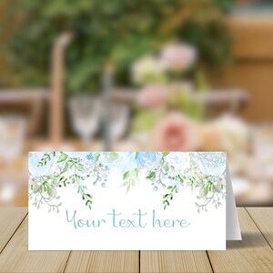 May include: A white place card with a blue watercolour floral design. The text "Your text here" is printed in blue at the bottom of the card.