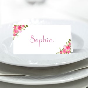 May include: White place card with pink floral designs on the corners and the name "Sophia" written in pink cursive.