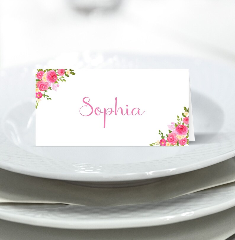 May include: White place card with pink floral designs on the corners and the name "Sophia" written in pink cursive.