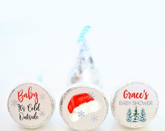May include: Three silver foil-wrapped chocolate candies with festive Christmas-themed labels. The labels feature a red Santa hat, a snowy forest scene, and the text "Baby It's Cold Outside".